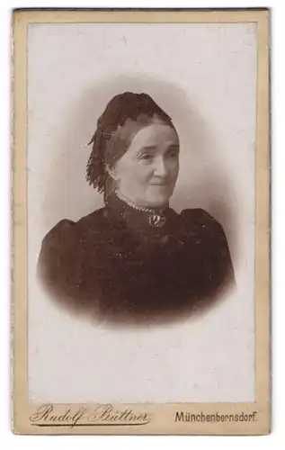Fotografie Rudolf Büttner, Münchenbernsdorf, Lächelnde ältere Dame mit Kopfbedeckung und Brosche