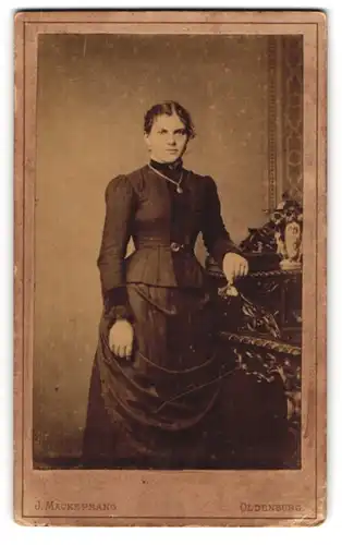 Fotografie J. Mackeprang, Oldenburg, Elegante junge Dame mit Seitenscheitel und Kette im taillierten Kleid