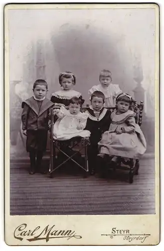 Fotografie Carl Mann, Steyr, sechs kleine Kinder in Kleidern posieren im Atelier