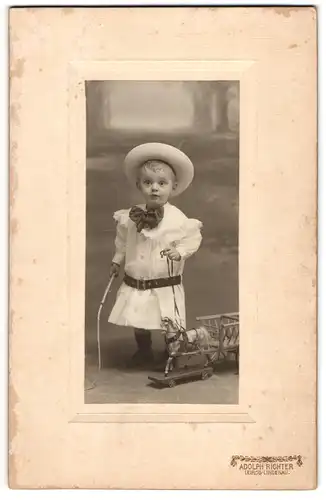 Fotografie Adolph Richter, Leipzig, niedliches Kind im Kleid mit Spielzeug Pferd und Peitsche