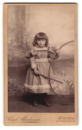 Fotografie Carl Machmar, Kassel, Unt. Königstr. 63, Portrait niedliches Mädchen im Kleid mit Stab und Reifen spielend