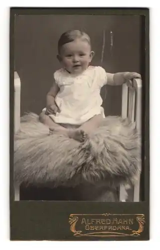 Fotografie Alfred Hahn, Oberfrohna, Portrait süsses Baby im Kleidchen auf einem Fell sitzend