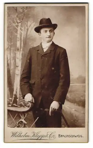 Fotografie Wilhelm Klopp & Co., Braunschweig, Friedrich Wilhelmstrasse 37, Junger Mann in Anzug und Hut vor Landschaft