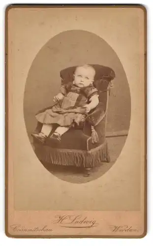 Fotografie Herm. Ludwig, Crimmitschau, Thieme-Strasse 73, Kleinkind in Kleid und Lackschühchen auf einem Sessel
