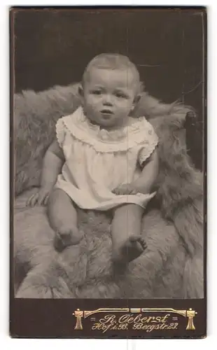 Fotografie R. Oeberst, Hof i. B., Bergstr. 23, Süsses Kleinkind im Hemd sitzt auf einem Fell