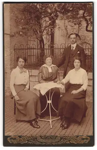 Fotografie unbekannter Fotograf und Ort, Drei Damen und eleganter Herr am Tisch in einem Hof