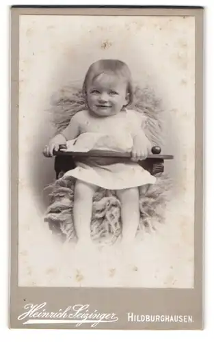 Fotografie Heinrich Seizinger, Hildburghausen, Lachendes Kleinkind auf einem Fell
