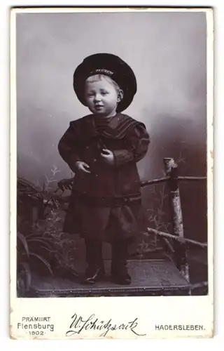 Fotografie W. Schützsack, Hadersleben, Bischofstr. 368, Kleines Kind im Matrosenkleid mit Mützenband