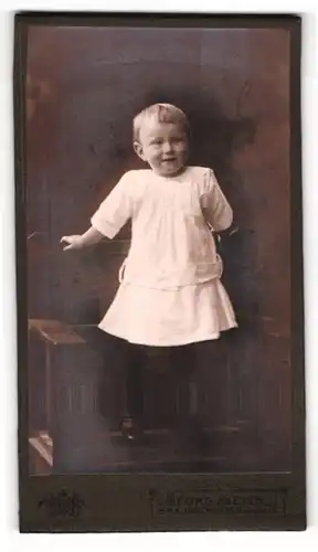 Fotografie Georg Meyer, Braunschweig, Bankplatz 3, Lächelndes kleines Kind im weissen Kleid