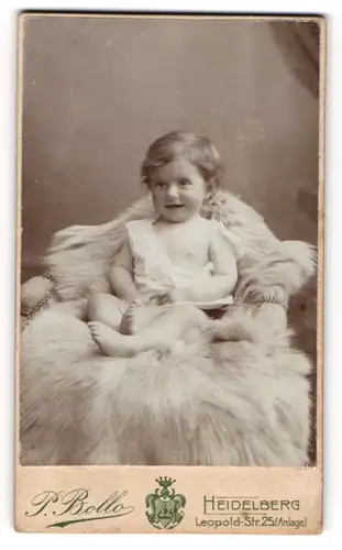 Fotografie P. Bollo, Heidelberg, Leopold-Str.25, lächelndes Kind auf pelzbedecktem Stuhl