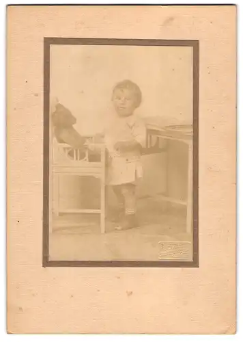 Fotografie unbekannter Fotograf und Ort, niedlicher kleiner Knabe mit seinem Teddybär auf dem Stuhl, 1919