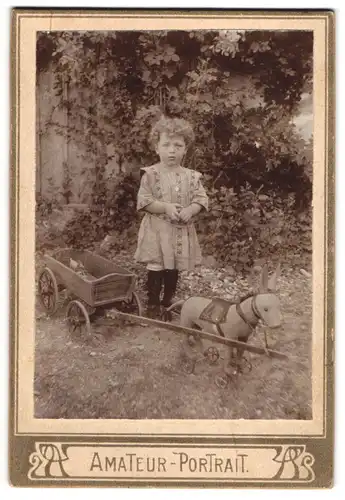 Fotografie unbekannter Fotograf und Ort, süsses Mädchen mit ihrem Stoff-Esel auf Rädern samt Anhänger im Garten