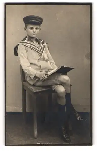 Fotografie unbekannter Fotograf und Ort, Portrait junger Knabe Fritz Hornung in Schuluniform mit Lehrbuch auf dem Schoss