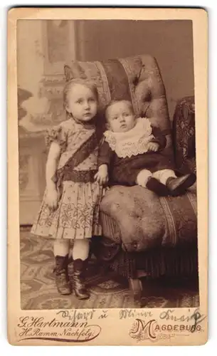 Fotografie G. Hartmann, Magdeburg, Lüneburgerstrasse 2, Mädchen in gemustertem Kleid mit Kleinkind auf einem Sessel