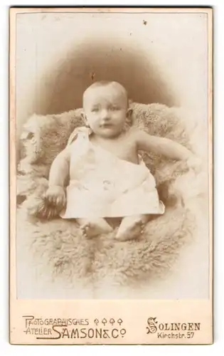 Fotografie Samson & Co., Solingen, Kirchstrasse 57, Zufrieden blickendes Baby auf einem Lammfell