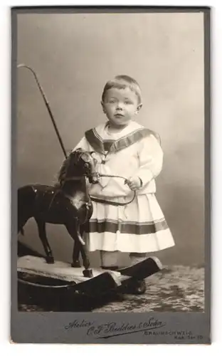 Fotografie C. F. Beddies & Sohn, Braunschweig, Kleinkind im Kleidchen mit Schaukelpferd und Peitsche