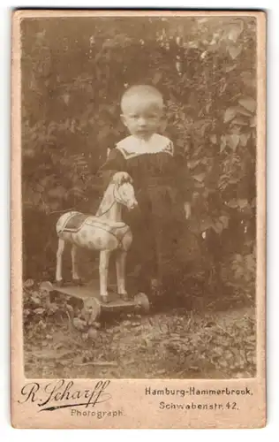 Fotografie R. Scharff, Hamburg, Kleinkind im Kleid mit Holzpferd auf Rädern