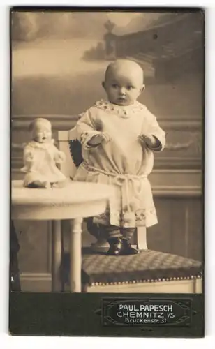 Fotografie Paul Papesch, Chemnitz, Kleinkind schaut erschrocken zur Puppe auf dem Tisch