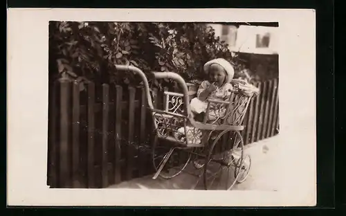 Foto-AK Kleines Kind im Kinderwagen vor einem Gartenzaun