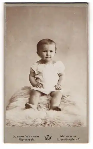 Fotografie Joseph Werner, München, Isarthorplatz 2, Portrait süsses Baby im weissen Hemdchen auf Fell sitzend