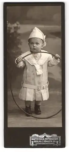 Fotografie Martin Balg, Berlin, Portrait niedlicer Knabe im gestreiften Kleid mit Zipfelmütze