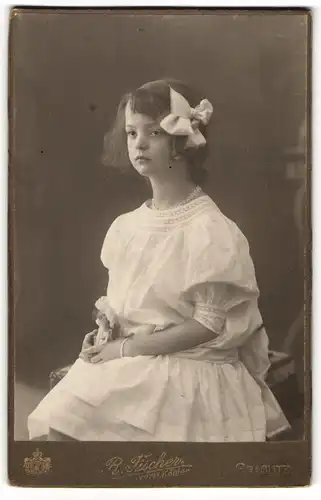 Fotografie R. Fischer, Graslitz, hübsches Mädchen im weissen Kleid mit Haarschleife schaut emotionslos