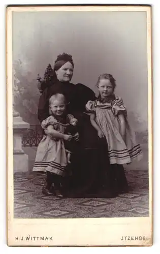 Fotografie H. J. Wittmak, Itzehoe, Grossmutter posiert stolz mit ihren beiden Enkeltöchtern im Atelier, Mutterglück