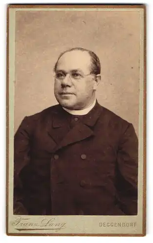 Fotografie Franz Lang, Deggendorf, Pastor im Anzug mit Collar und Brille