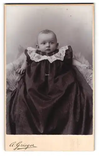 Fotografie A. Grieger, Berlin, Friedens-Strasse 8, Baby im dunklen Taufkleid mit Spizenkragen auf einem Fell