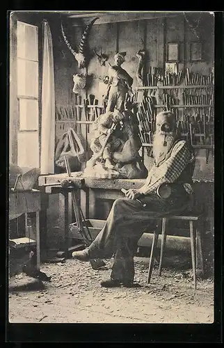 AK Holzbildhauer mit Stemmeisen vor einer Skulptur in seiner Werkstatt