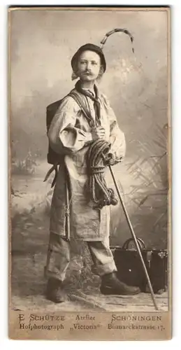 Fotografie E. Schütze, Schöningen, junger Knabe als Wanderer mit Seil, Wanderstock und Koffer, angeklebeter Bart