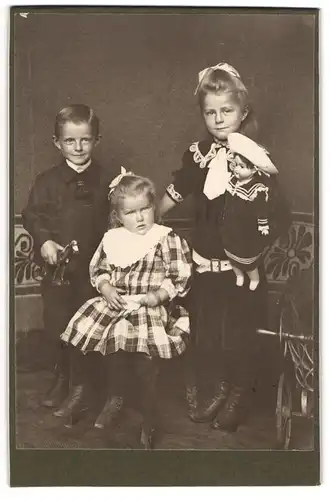 Fotografie unbekannter Fotograf und Ort, drei niedliche Kinder mit Puppe in der Hand und Knabe mit Spielzeug Pferd