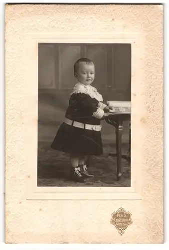 Fotografie Ferd. Eggeling, Witten, Lächelndes Kleinkind im Kleidchen mit Gürtel und Stiefelchen