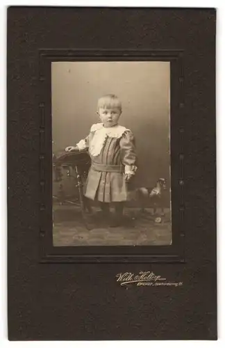Fotografie Wilhelm Holtorp, Bremen, Osterthorsteinweg 61, Kleinkind mit Ponyfrisur im Kleidchen, mit Spielzeugpferd