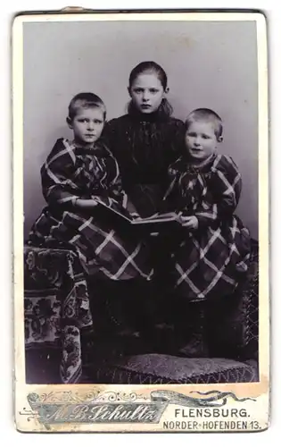Fotografie M. B. Schultz, Flensburg, Norder-Hofenden 13, Drei Kinder in modischen Kleidern mit Album