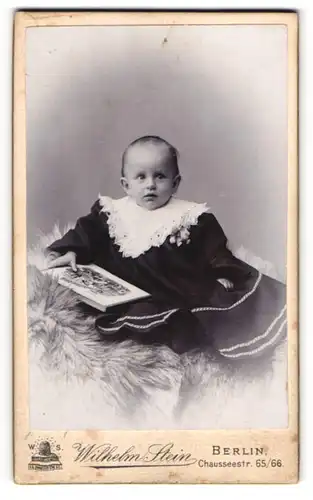Fotografie Wilhelm Stein, Berlin, Chausseestr. 65-66, Süsses Kleinkind im Kleid mit Bilderbuch