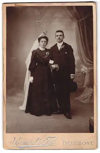 Fotografie J. Enard, & Fils, Delemont, junges Ehepaar im schwarzen Brautkleid mit Schleier, Herr im Anzug mit Melone