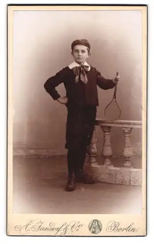 Fotografie A. Jandorf & Co., Berlin, Grosse Frankfurterstr. 113, Modisch gekleideter Junge mit Tennisschläger