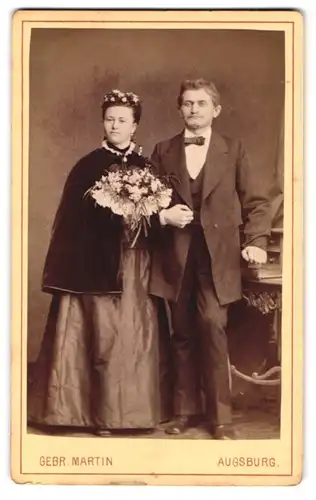 Fotografie Gebr. Martin, Augsburg, Eheleute im dunklen Brautkleid mit Samtüberwurf und im Anzug