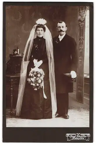 Fotografie Josef Schäffer, Kempten, Ehepaar im schwarzen Brautkleid und im Anzug mit Zylinder, Brautstrauss