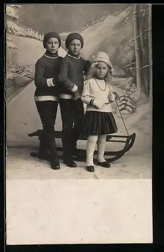AK Zwei Buben und ein Mädchen mit Schlitten vor einer verschneiten Studiokulisse