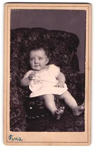 Fotografie unbekannter Fotograf und Ort, Vergnügtes Kleinkind im Strampelkleid auf einem Sessel