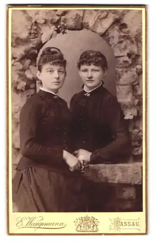 Fotografie E. Wangermann, Passau, zwei junge Damen in dunklen Kleidern posieren in einer Studiokulisse