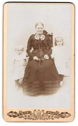 Fotografie unbekannter Fotograf und Ort, Portrait Grossmutter mit ihren beiden Enkelkindern im Atelier
