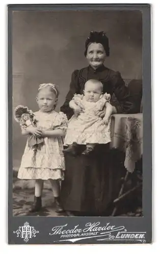 Fotografie Theodor Harder, Lunden, Grossmutter mit ihren beiden Enkelkindern samt Puppe im Arm