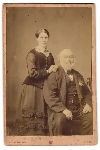 Fotografie J. Sunderland, Wolverhampton, Queen St. 53, Äterer Herr mit weissem Vollbart und ältere Dame mit Brosche