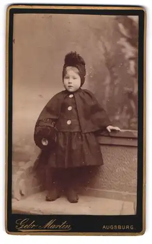 Fotografie Gebr. Martin, Augsburg, niedliches kleines Mädchen im Winterkleid mit Muff