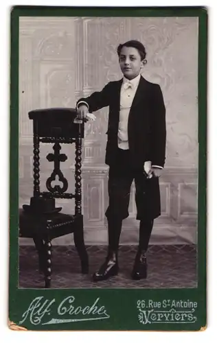 Fotografie Alf. Croche, Verviers, junger Knabe im Anzug mit halb langer Hose und Fliege, Lackschuhe