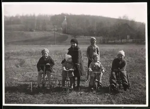 Fotografie Kinder mit Dreirad & Tretauto sielen auf einer Wiese