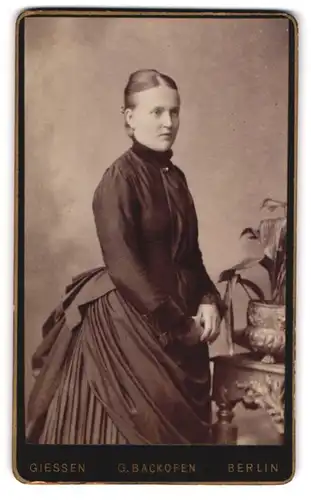 Fotografie Gustav Backofen, Berlin, Mohrenstr. 63 /64, Gutbürgerliche Dame in schwarzem Kleid mit Pflanze